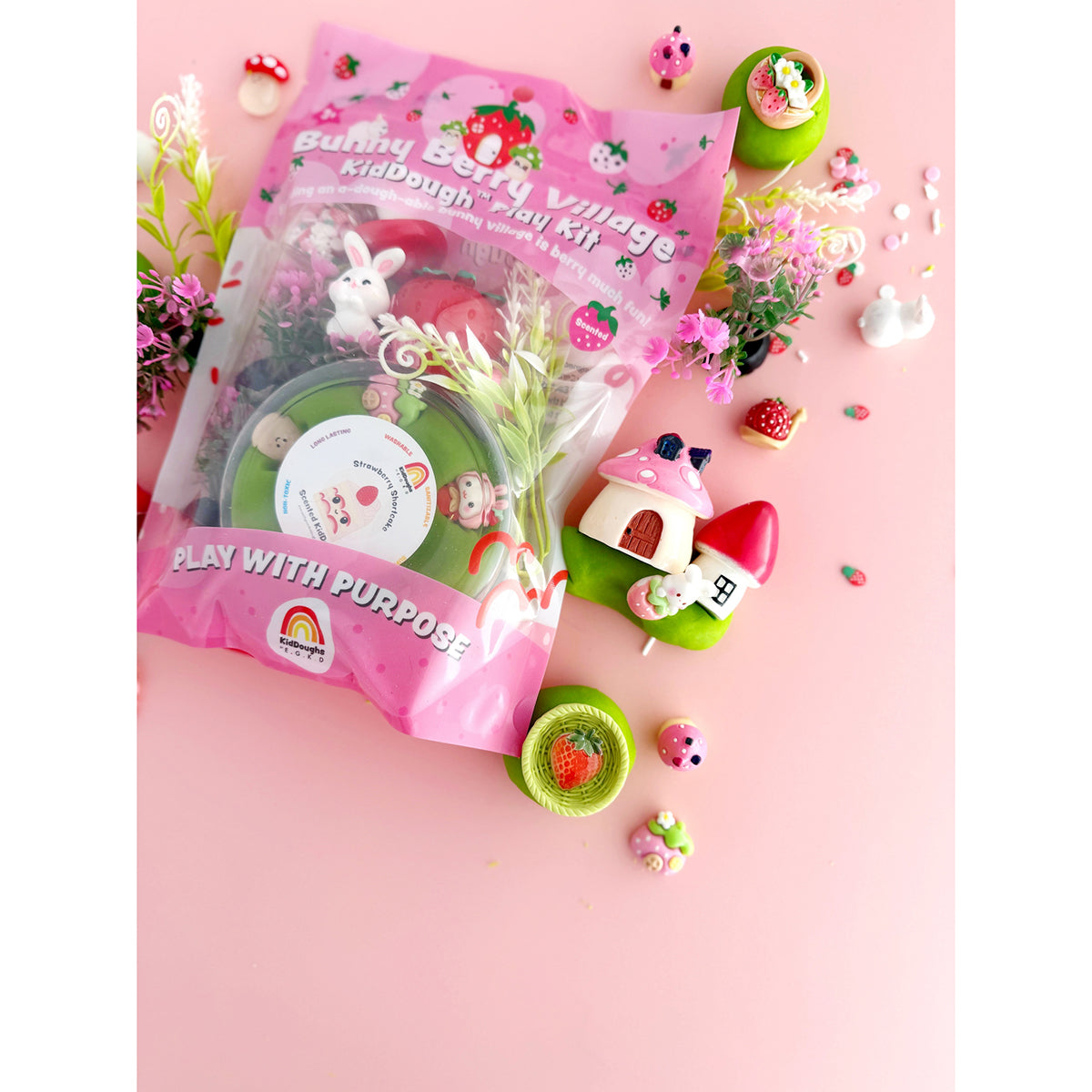 Earth Grown KidDoughs Bunny Berry Village KidDough Sensory Play Kit packaging on a pink background with play pieces scattered around it.