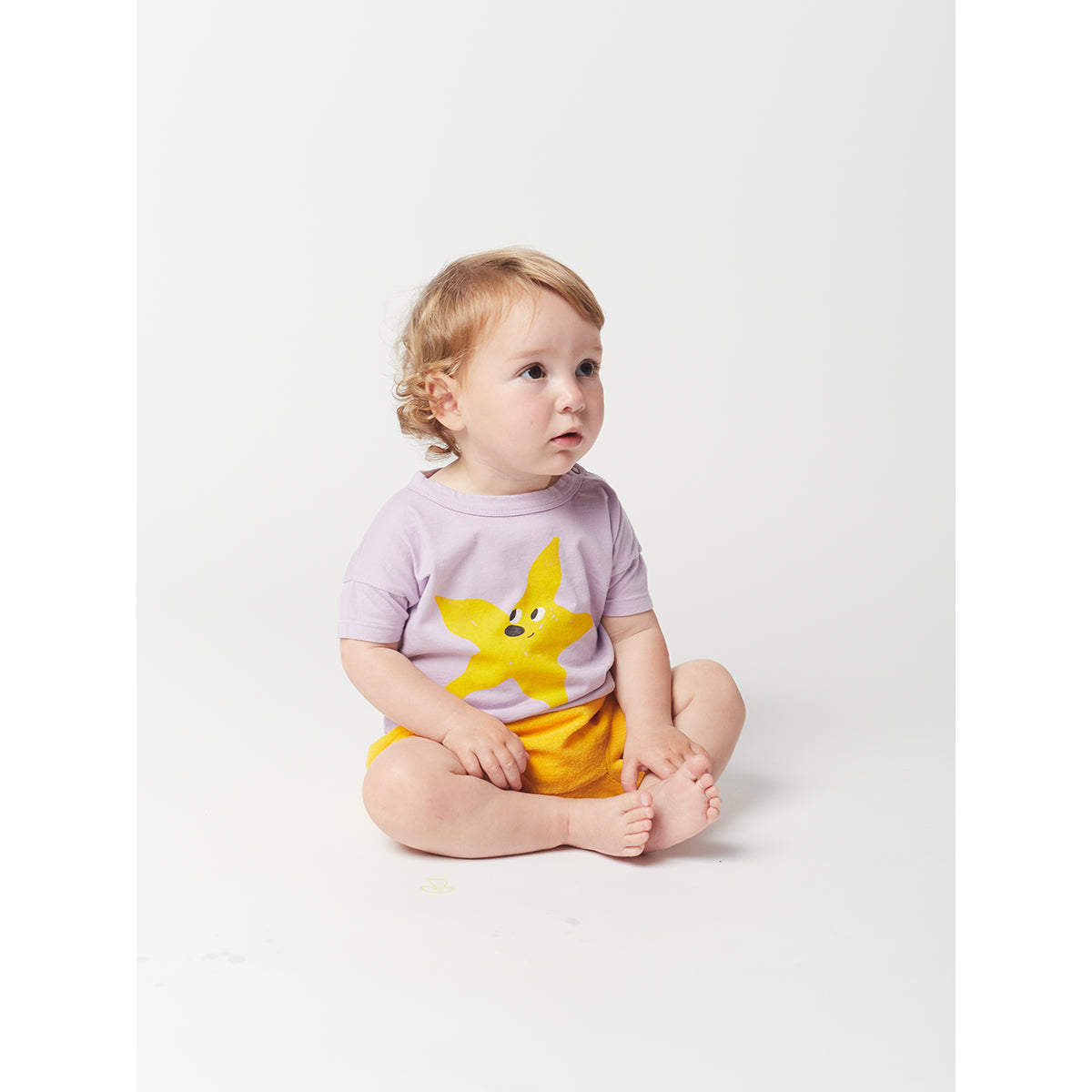 yellow starfish print on front on a lavender t-shirt with short sleeves and dropped shoulder and shoulder snap fastening from bobo choses for babies and toddlers