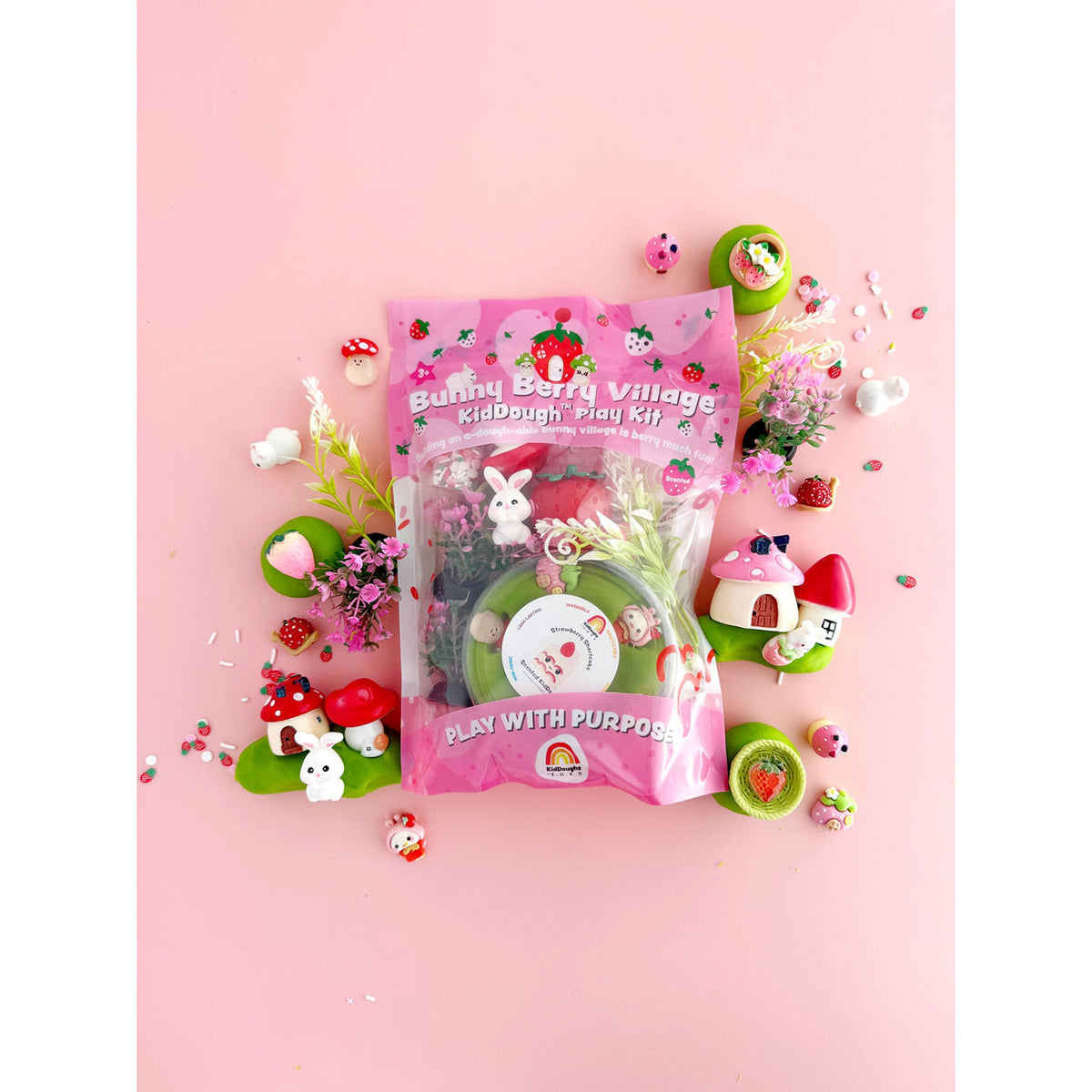 Earth Grown KidDoughs Bunny Berry Village Sensory KidDough Play Kit on a pink background with toy play pieces scattered around the packaging.