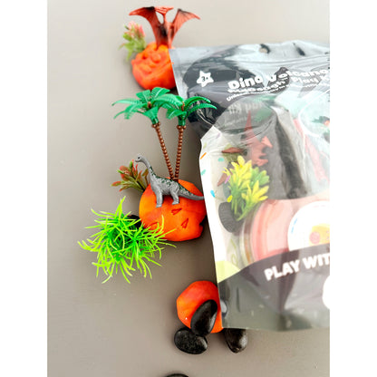 Dinosaurs, trees and rocks on red/orange marbled KidDough and the left side of the EGKD Dino Sensory KidDough Play Kit packaging on a grey background.